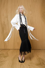 Falda negra con corte diagonal y flecos, llevada por modelo con camisa blanca